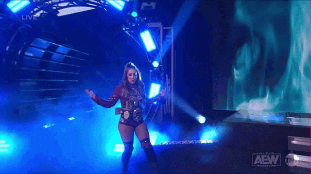 a woman in a red and black outfit is walking in a dark room with a aew logo on the screen .