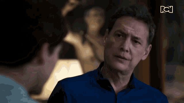a man in a blue shirt is talking to another man in front of a picture .