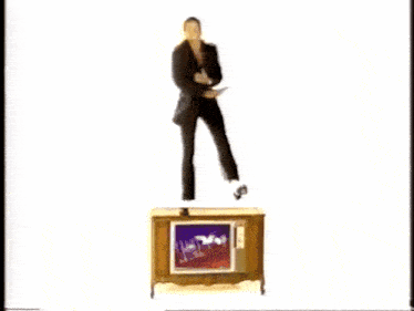 a man in a suit is jumping over a television