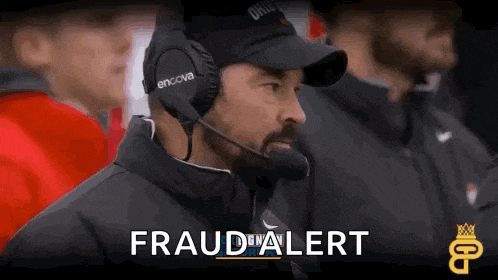a man wearing headphones and a microphone is watching a football game and says fraud alert .
