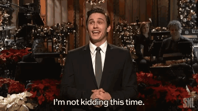 a man in a suit and tie says i 'm not kidding this time in front of christmas decorations