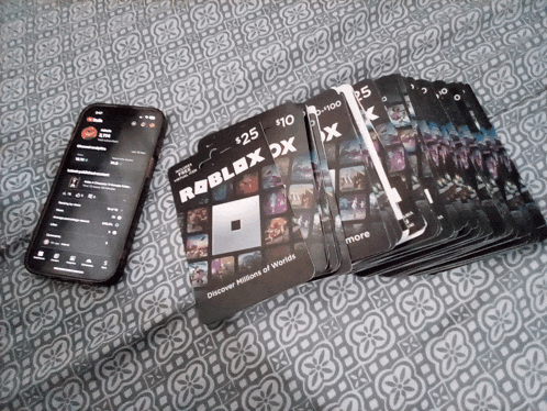 a stack of roblox dx gift cards next to a phone