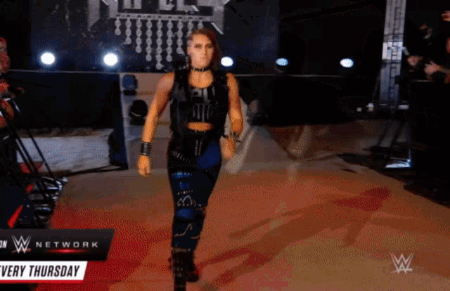 a female wrestler walks down a red carpet in front of a sign that says ' very thursday '