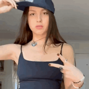 a woman wearing a hat and a tank top is pointing her finger at the camera .