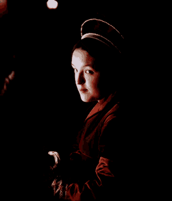 a woman wearing a hat and a red jacket looks at something in the dark