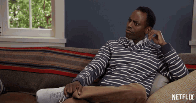 a man in a striped shirt sits on a couch with netflix written on the bottom