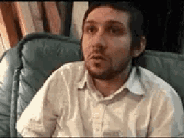 a man with a beard is sitting in a chair looking at the camera .