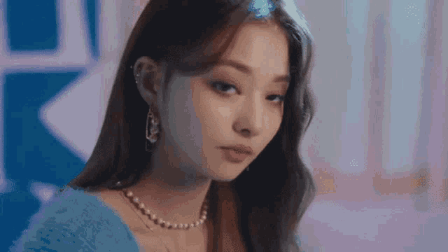 a close up of a woman wearing a blue sweater and pearls .