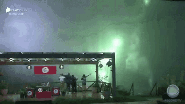 a group of people are standing in front of a building with a green light coming out of the roof .