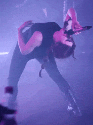 a woman is upside down holding a pink microphone