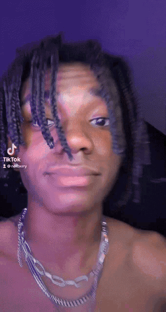 a man with dreadlocks is wearing a necklace and has a tiktok sticker on his face