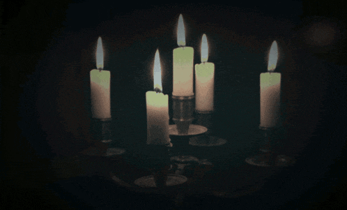 five candles are lit in a candle holder in the dark