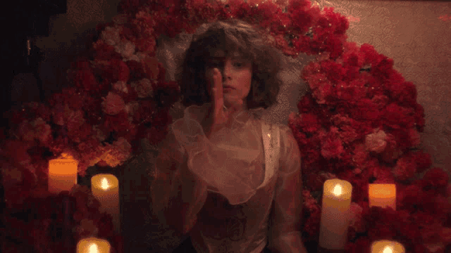 a woman sitting in front of a wreath of red flowers with candles