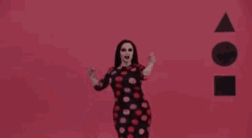 a woman in a polka dot dress is dancing in front of a red background with geometric shapes .