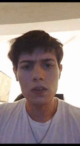a young man wearing a white t-shirt and a chain around his neck is making a funny face