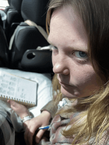 a woman sits in a car with a notebook and a pen in her hand