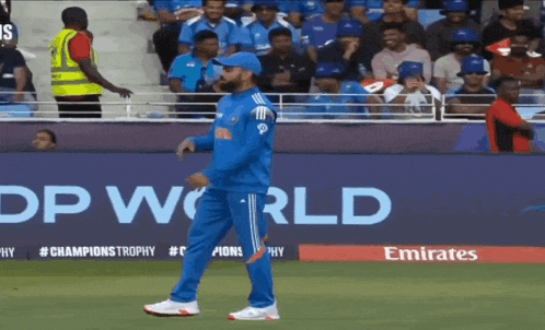 a man in a blue uniform is walking on a field in front of a emirates ad