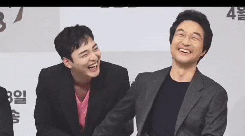 two men are laughing together while sitting next to each other on a stage .