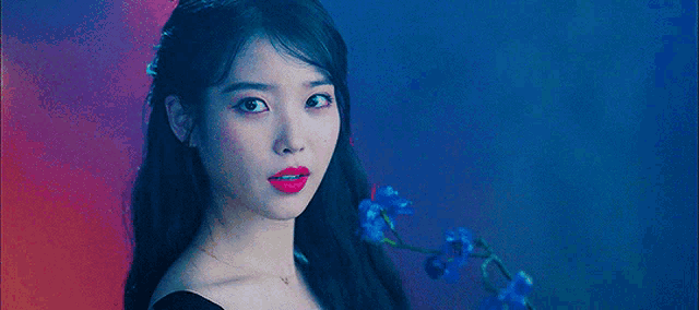a woman in a black dress is holding a blue flower and wearing red lipstick .