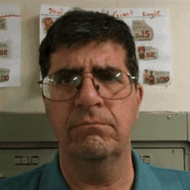 a man wearing glasses is making a funny face in front of a sign that says giant eagle on it .