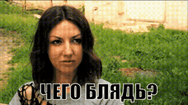 a woman in a gray shirt stands in a grassy field with the words " чего блядь " on the bottom right