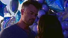 a man and a woman are kissing in front of a bunch of balloons .