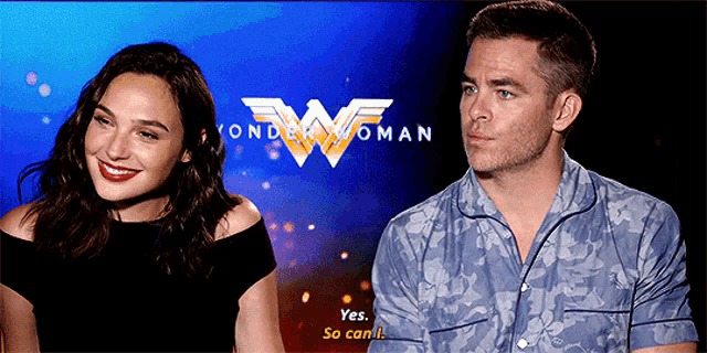 a man and a woman are sitting in front of a wonder woman sign