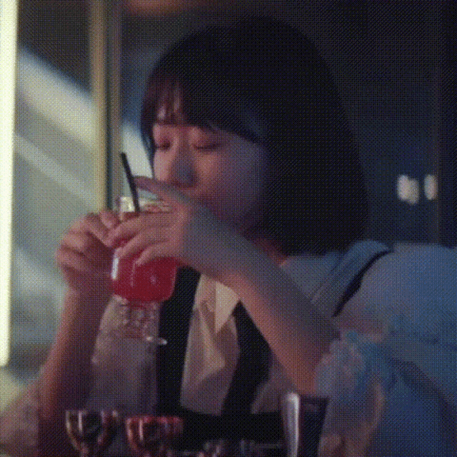 a woman is drinking a red drink with a straw from a bottle .