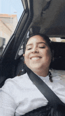 a woman wearing a white shirt and black skirt smiles while sitting in a car