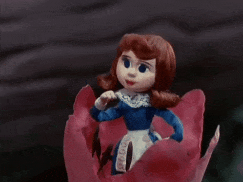 a doll in a blue dress is sitting on a flower