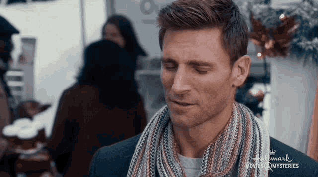 a man wearing a scarf and a jacket is standing in front of a crowd .