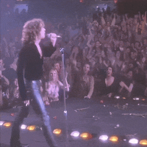 a woman singing into a microphone with a crowd behind her