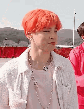 a man with red hair wearing a pink shirt and a white jacket