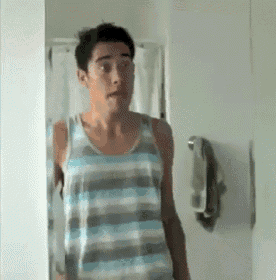 a man in a striped tank top stands in front of a bathroom mirror