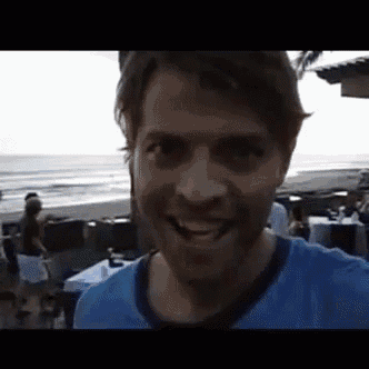 a man in a blue shirt is smiling while standing on a beach