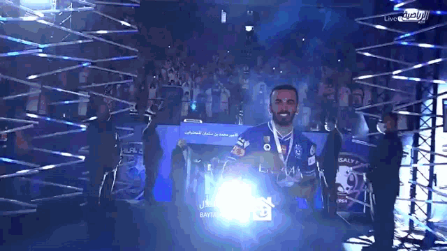 a man in a blue shirt holds a trophy in front of a crowd that says ' live ' on the bottom