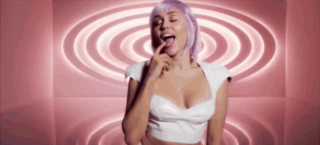 a woman with purple hair and a white top has her tongue out