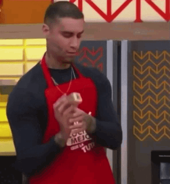 a man wearing a red apron and a black shirt is standing in front of a fridge .