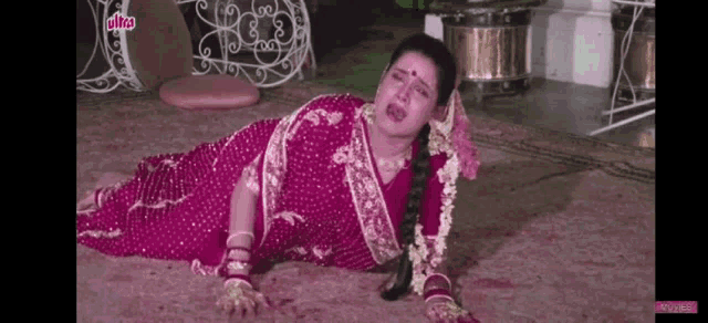 a woman in a pink saree is laying on the floor .