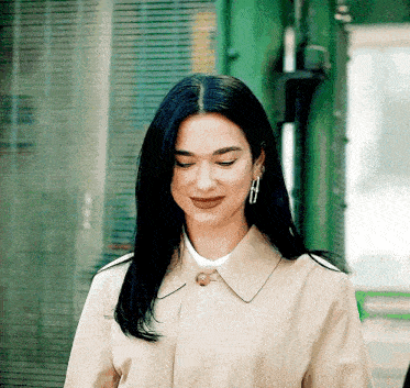 a woman wearing a trench coat and earrings is standing in front of a green building .