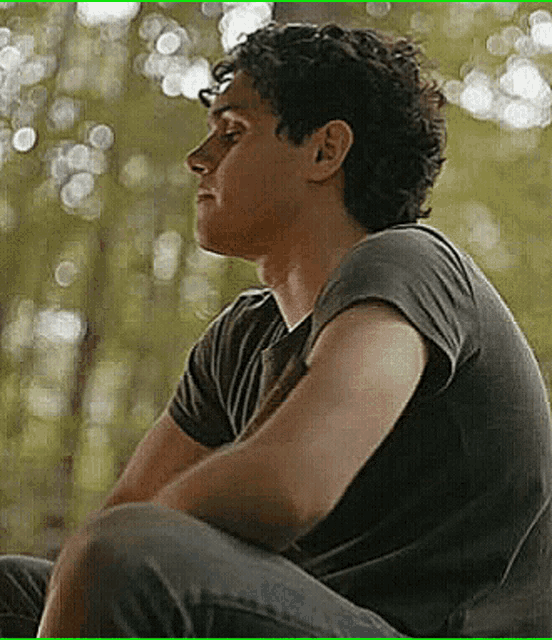 a man in a black shirt is sitting in the woods with his eyes closed .