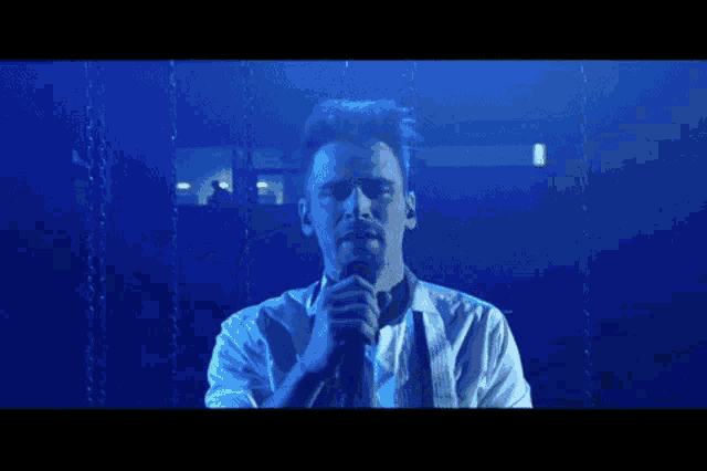 a man in a white shirt is singing into a microphone in front of a blue background .