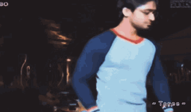 a man in a blue and white shirt is standing in a dark room with the word toree below him