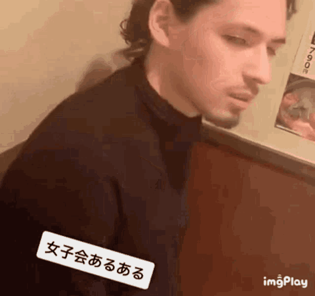 a man with a beard and a black turtleneck is sitting in a room .