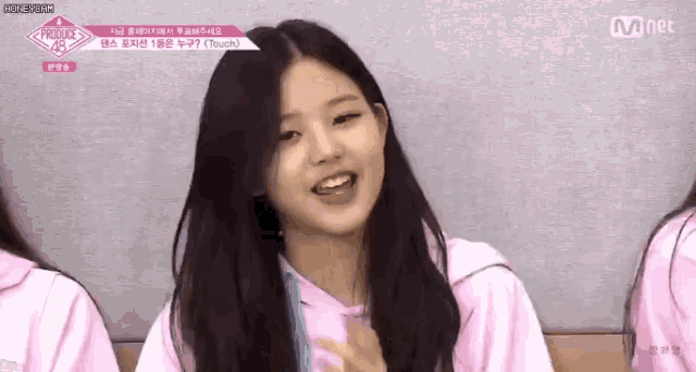 a girl in a pink shirt is smiling and looking at the camera while sitting in front of a group of girls .