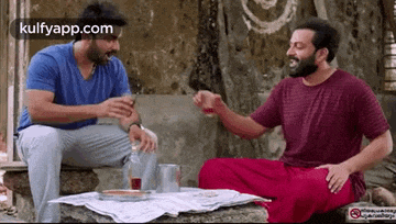 two men are sitting at a table talking to each other and drinking alcohol .