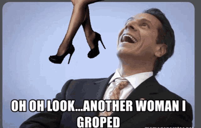 a man in a suit and tie laughs while looking up at a woman 's legs hanging from the ceiling