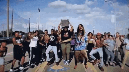 a group of people are dancing on a sidewalk while a man holds a box over his head .