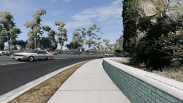a white car is driving down a road next to a brick wall