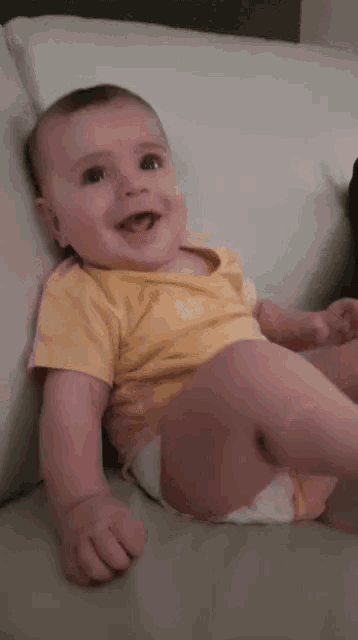 a baby laying on a couch with a yellow shirt that says ' baby ' on it